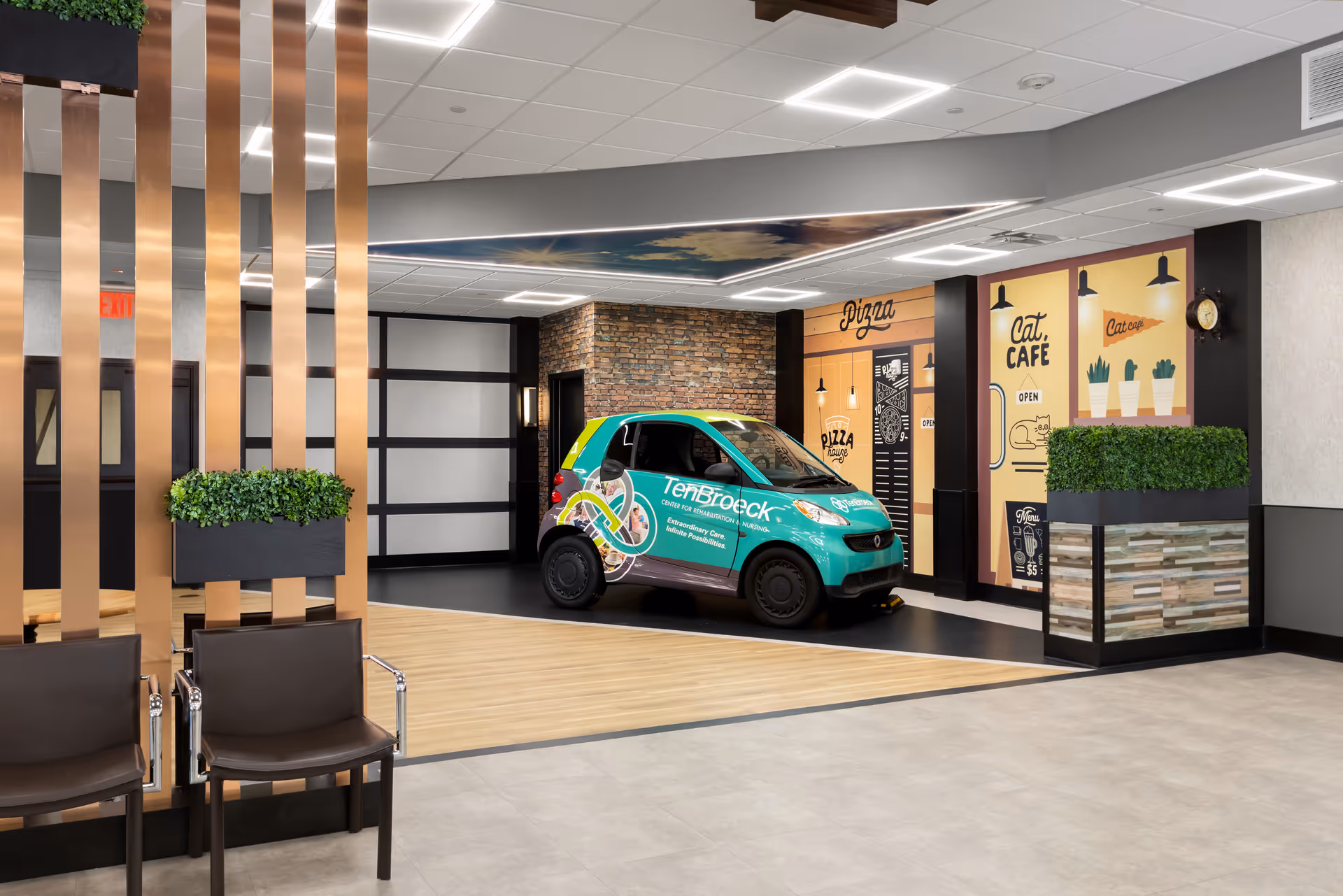 Indoor area of a facility with modern decor including brown chairs, vertical copper-colored slats with green plants, and a small teal car branded with 'TenBroeck Center for Rehabilitation and Nursing' parked on a black and wood floor section. The background features a wall with brick accents and colorful murals advertising a pizza place and a cat cafe.