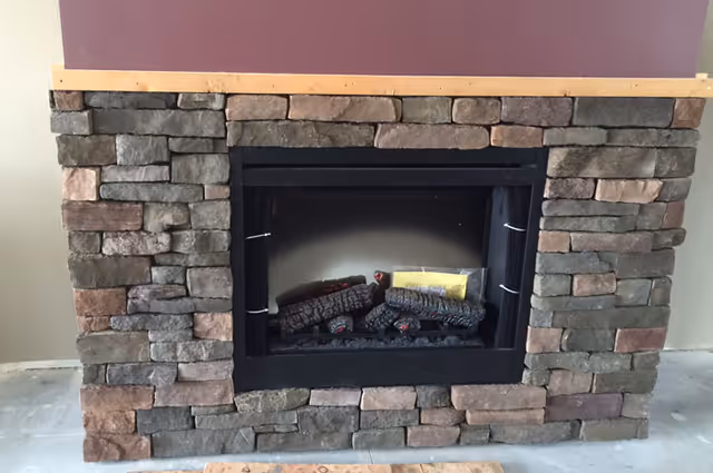 A stone fireplace with a black metal frame and artificial logs inside, set against a wall with a purple upper section and beige sides.
