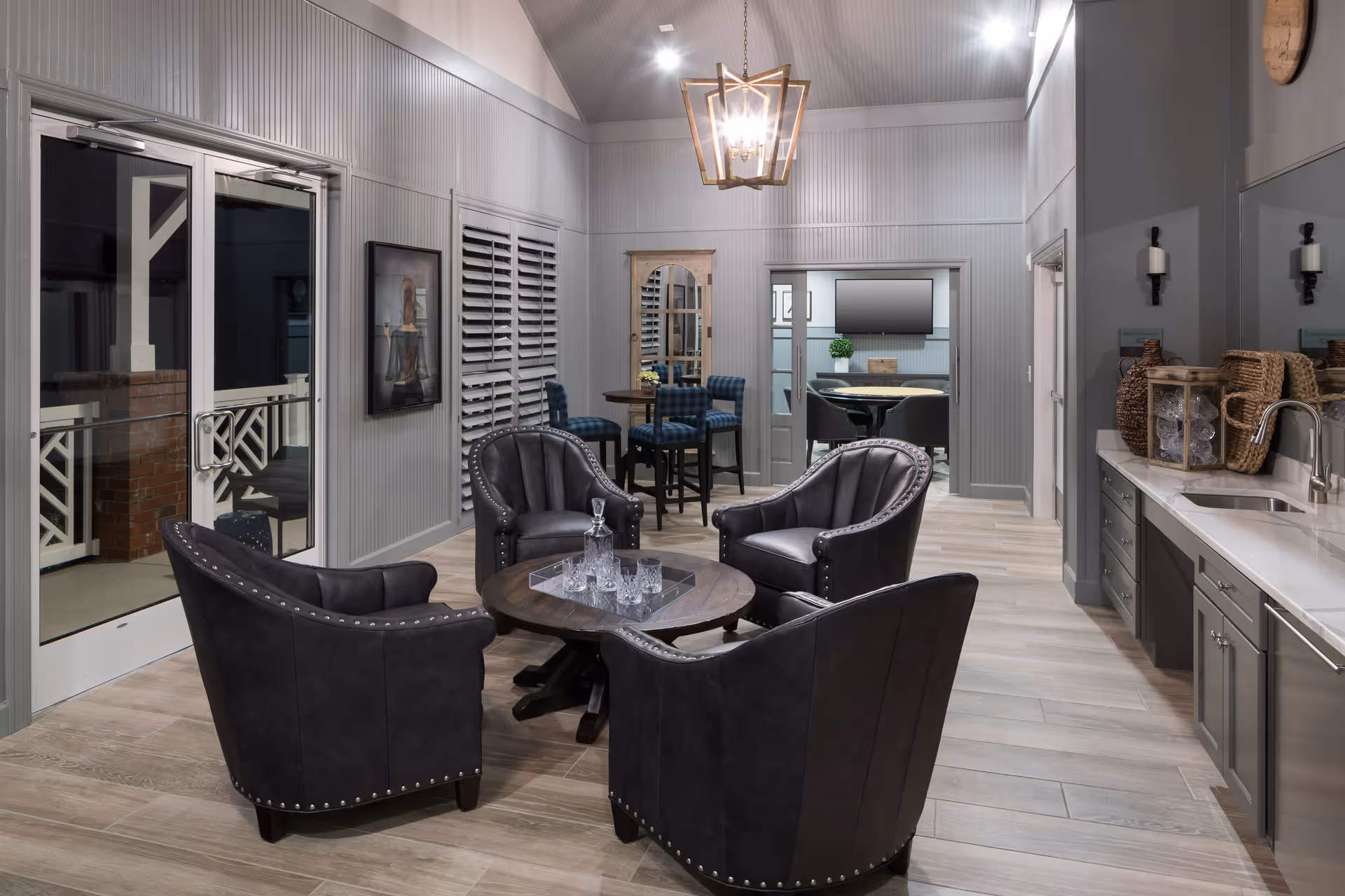 Communal lounge with four dark leather armchairs around a round coffee table, a kitchenette along the right wall, and a small dining area in the background.