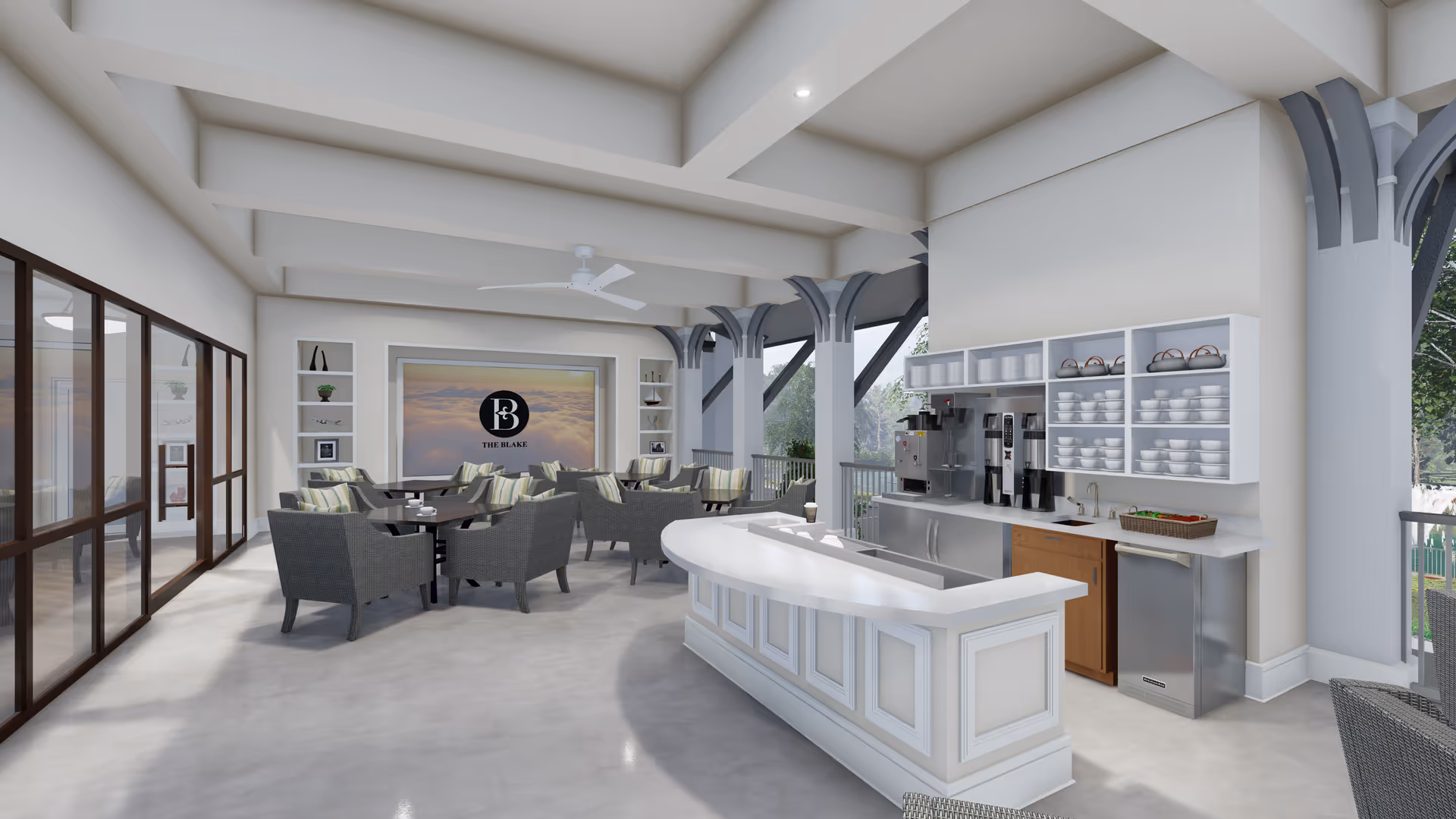 A bright and spacious indoor lounge area with a coffee bar on the right side, featuring coffee machines, cups, and a small sink. Several wicker chairs with cushions are arranged around dark tables in the center and left side of the room. The back wall displays a large framed image with the logo 'The Blake' and decorative shelves with small plants and ornaments. Large windows and open structural beams provide natural light and a view of greenery outside.