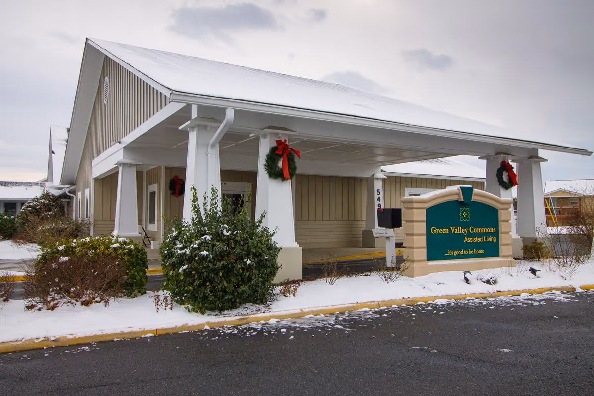 The snow-dusted entrance of Green Valley Commons assisted living with a covered porte-cochere, holiday wreaths, and a sign in front.