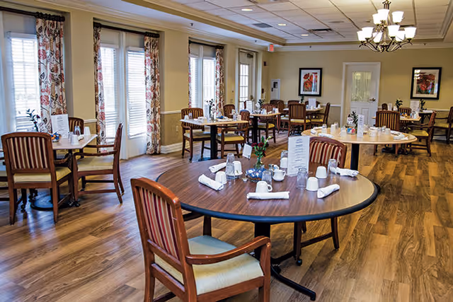 Bright dining room with round wooden tables and chairs set with place settings and napkins.