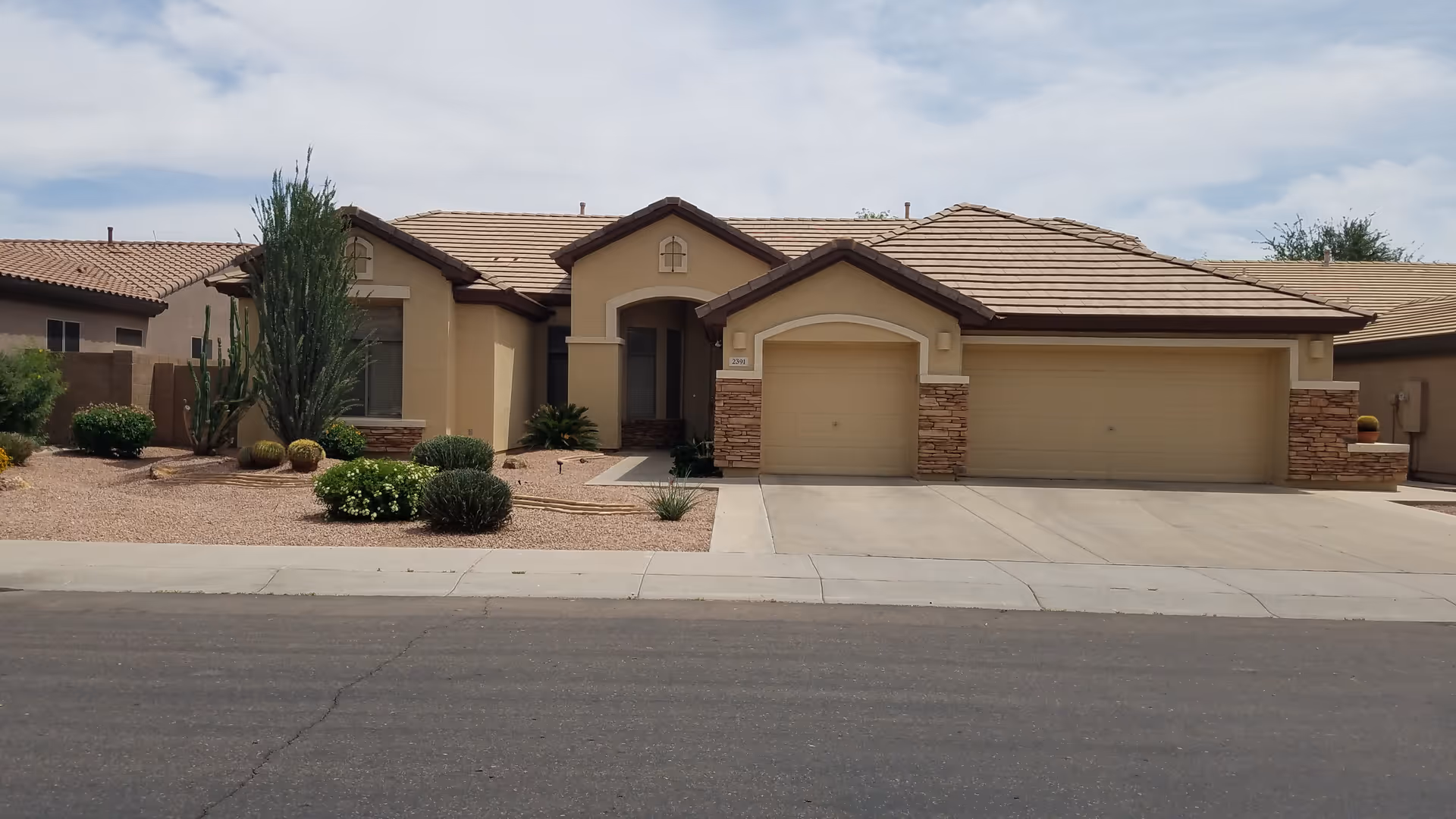 Single-story stucco house with a three-car garage, tiled roof and desert landscaping viewed from the street.