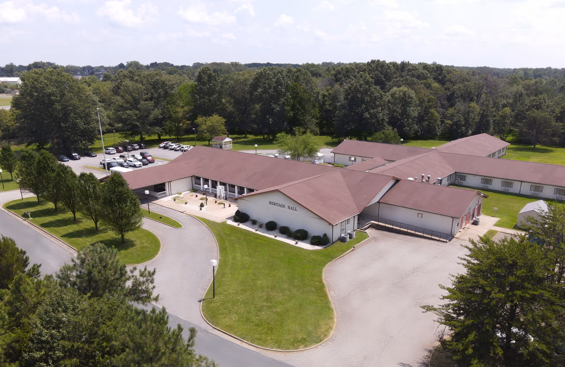 Aerial view of the single-story Heritage Hall Dillwyn building with red roofs, circular driveway, parking lot and surrounding trees.