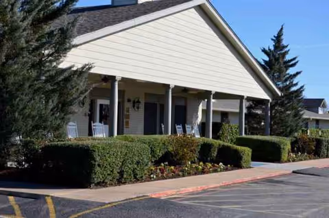 Exterior of a senior care facility with a covered porch, columns, and landscaped shrubs.