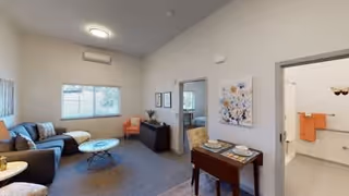 Bright furnished living room with a sofa, coffee table, small dining table and a view into an adjacent bathroom.