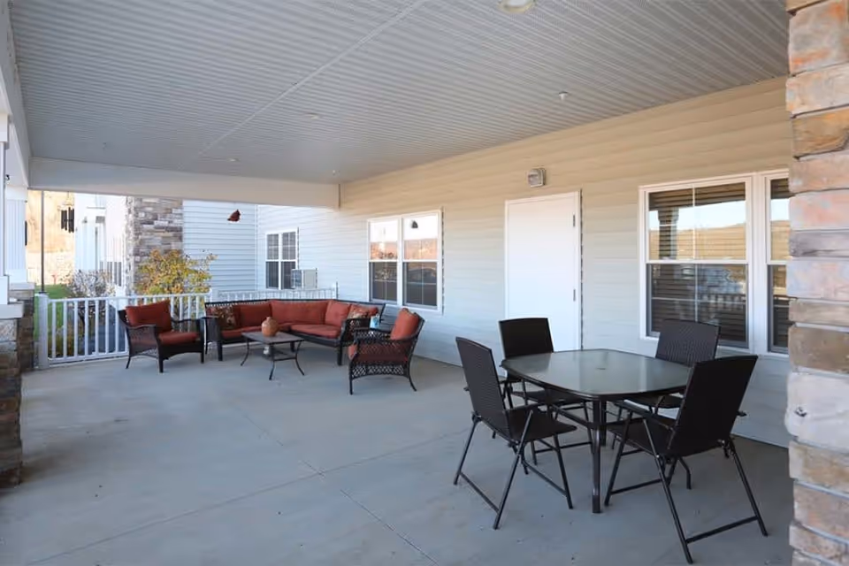 Covered outdoor patio with a glass-top dining table and chairs and a cushioned seating area under a porch.