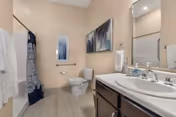 A clean bathroom with a sink and mirror, toilet, and a tub/shower with a patterned curtain.