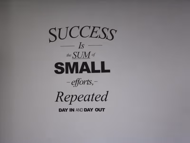 A motivational quote on a plain wall that reads: 'SUCCESS Is the SUM of SMALL efforts, Repeated DAY IN AND DAY OUT'.