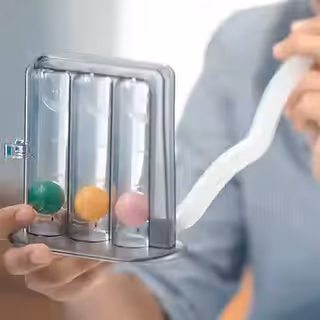 A hand holds a clear device with three vertical tubes containing colored spheres.