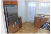 Small kitchen with stainless steel refrigerator and stove, wooden cabinets, sink, and a door with vertical blinds.