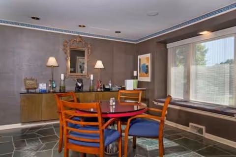 A dining area with a round table, wooden chairs, and lamps by a window.