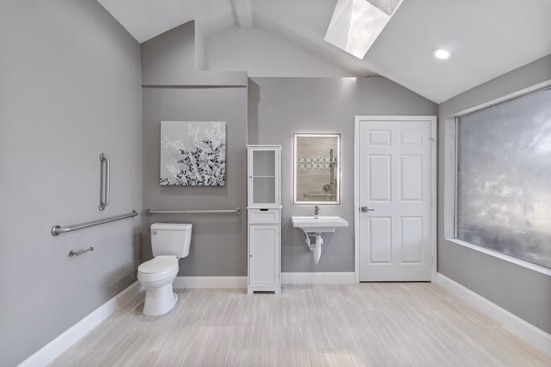 Accessible bathroom with a toilet, wall-mounted sink, storage cabinet, grab bars, and a large frosted window.