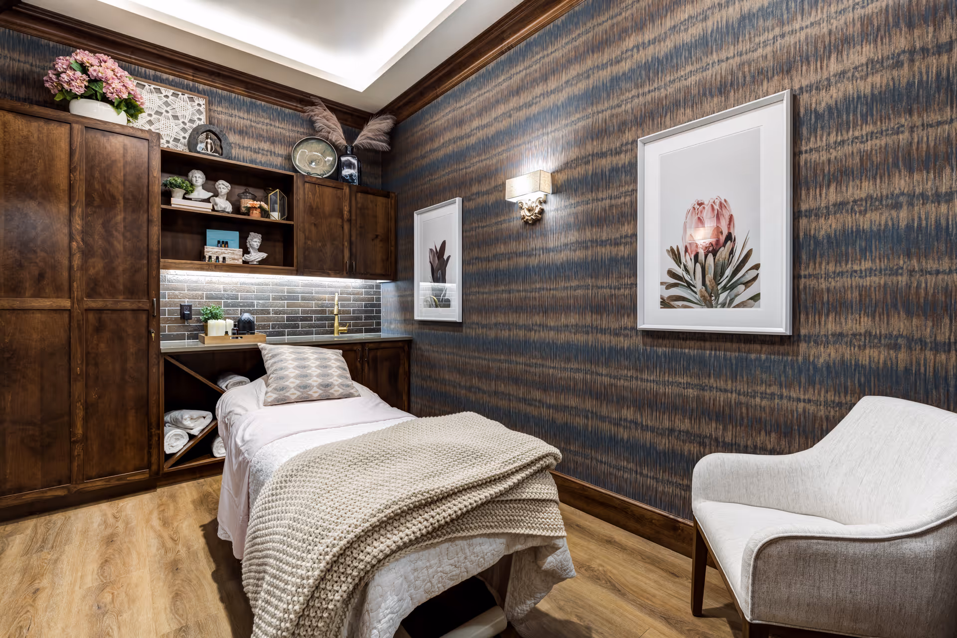 Cozy interior treatment room with a single bed, wooden cabinets, patterned wallpaper, and an armchair.