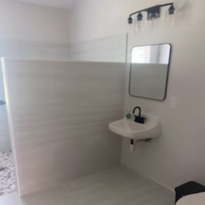 Small modern bathroom with a wall-mounted sink, mirror, light fixture and a half-wall shower partition.