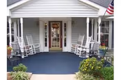 Front entrance of a senior living home with rocking chairs on a blue porch.