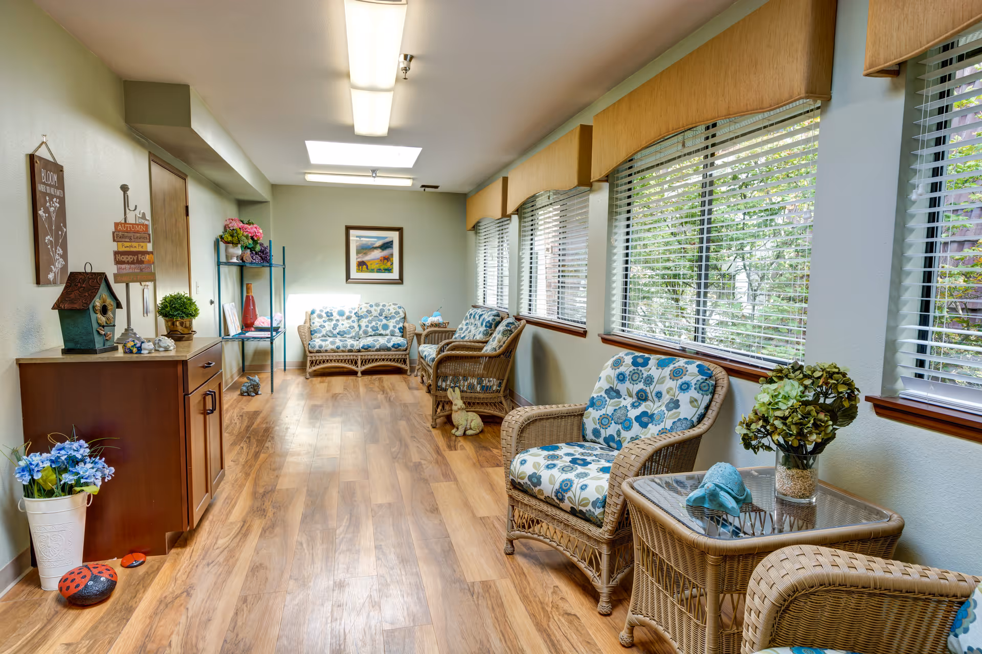 Bright sunroom-style lounge with wicker chairs and floral cushions along a windowed wall.