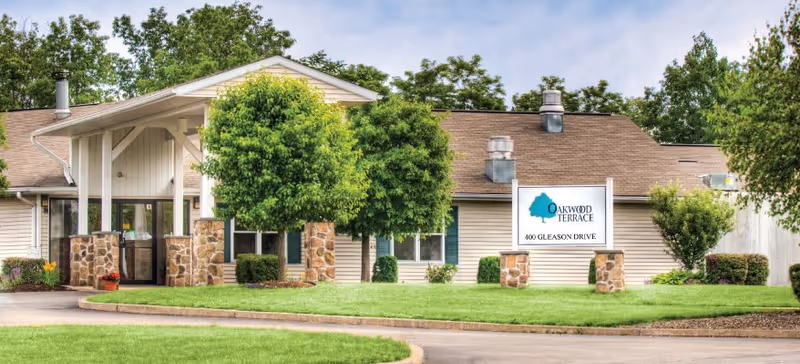 Oakwood Terrace senior living facility exterior with sign, green lawn, and trees.