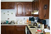A kitchen with wooden cabinets, a countertop with various items including a kettle on the stove, a dish rack with dishes, and some decorative items on the wall and counter.