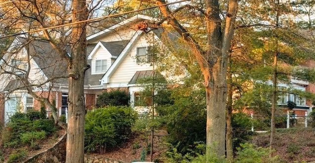 Exterior view of a senior living facility building partially obscured by trees and greenery in the foreground during autumn.