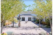 A paved walkway lined with trees and shrubs leading to a single-story building with a white exterior and a covered entrance, under a clear blue sky.