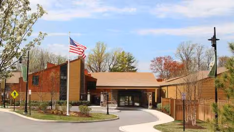 Front view of a brick senior living building with curved driveway and flagpole.
