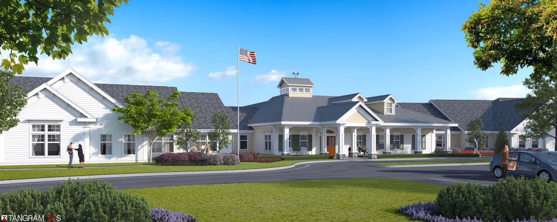 Exterior view of a single-story senior living facility building with white siding and a gray roof. The building features a covered entrance with columns, an American flag on a flagpole, and landscaped grounds with green grass, bushes, and trees. Several people are visible near the entrance and parking area under a clear blue sky.