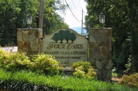 Stone entrance sign reads Four Oaks Health Care Center amid greenery.