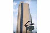 Tall beige high-rise building with a hanging sign against a blue sky.