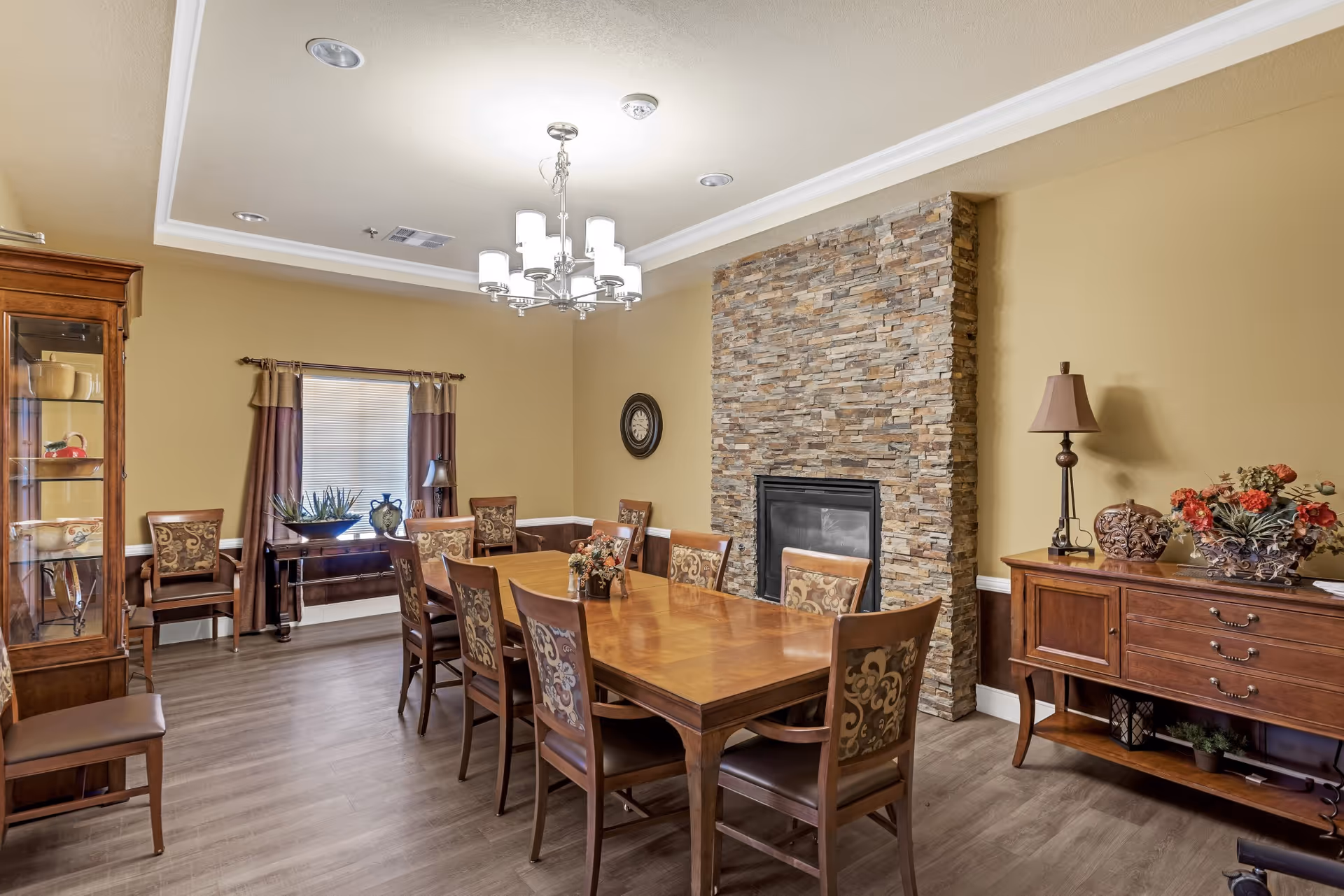 Well-appointed dining room with a long wooden table and chairs, stone fireplace, chandelier, and sideboard with decor.