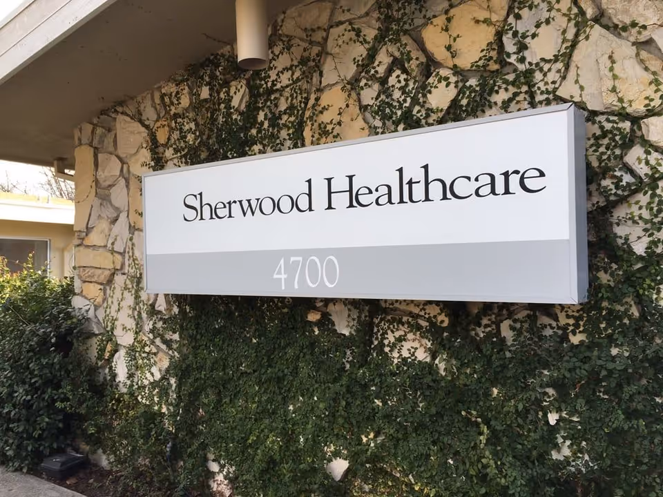 A Sherwood Healthcare sign reading "4700" mounted on a vine-covered stone exterior wall.