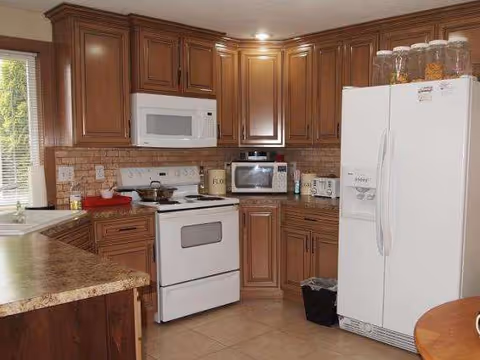 Compact kitchen with wooden cabinets, beige countertops, and white appliances.
