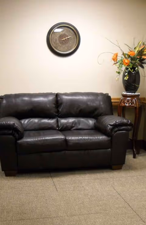 Black leather sofa, wall clock, and flower vase in a well-lit living room.