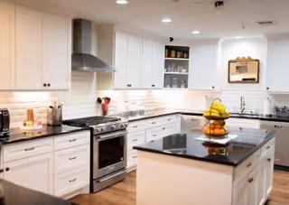 Bright modern kitchen with white cabinets, stainless steel appliances, a central island topped with a fruit bowl, and wood floors.
