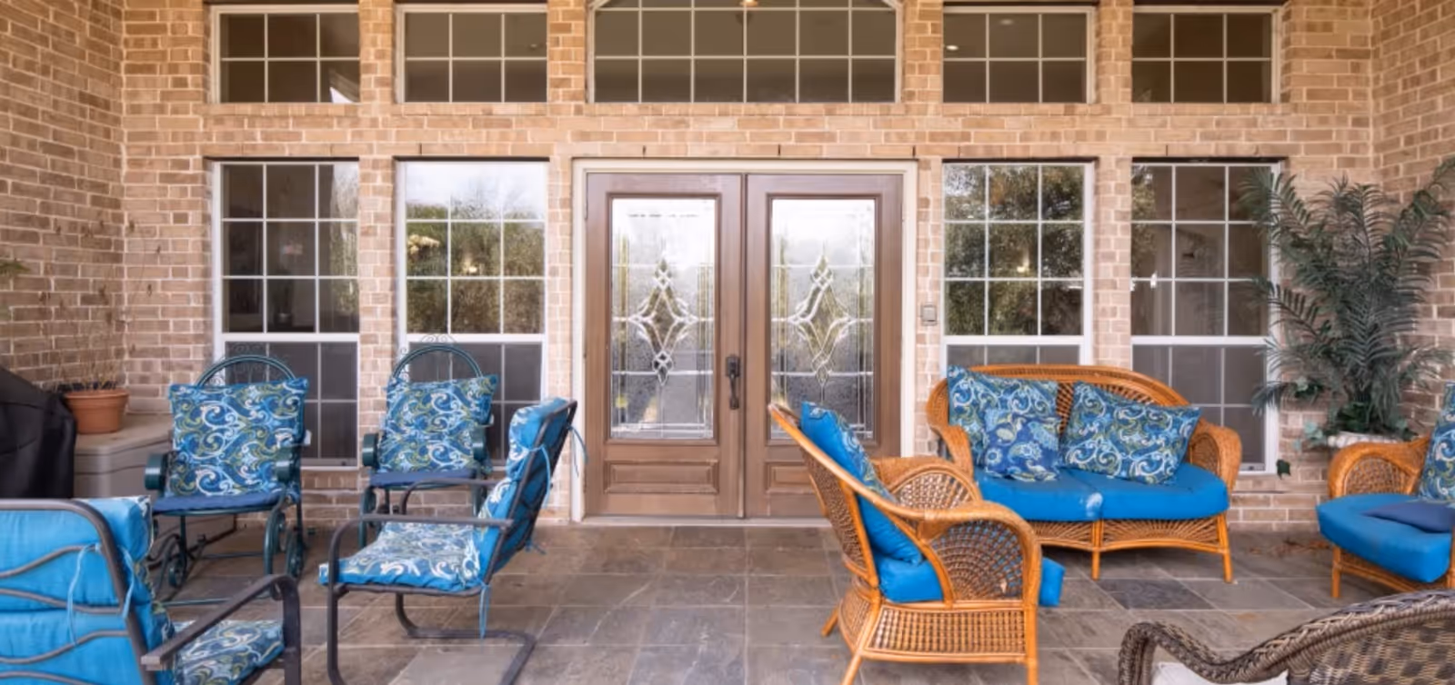 Covered brick patio with wicker and metal seating arranged around glass-paneled double doors.
