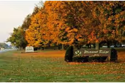 A Pleasant Ridge entrance sign on a grassy lawn with autumn trees along a road.