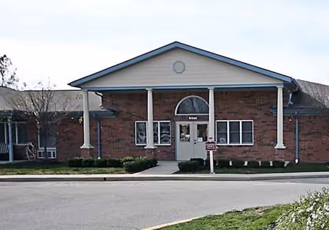 Brick senior living facility front entrance with columns and a rounded window above doors.