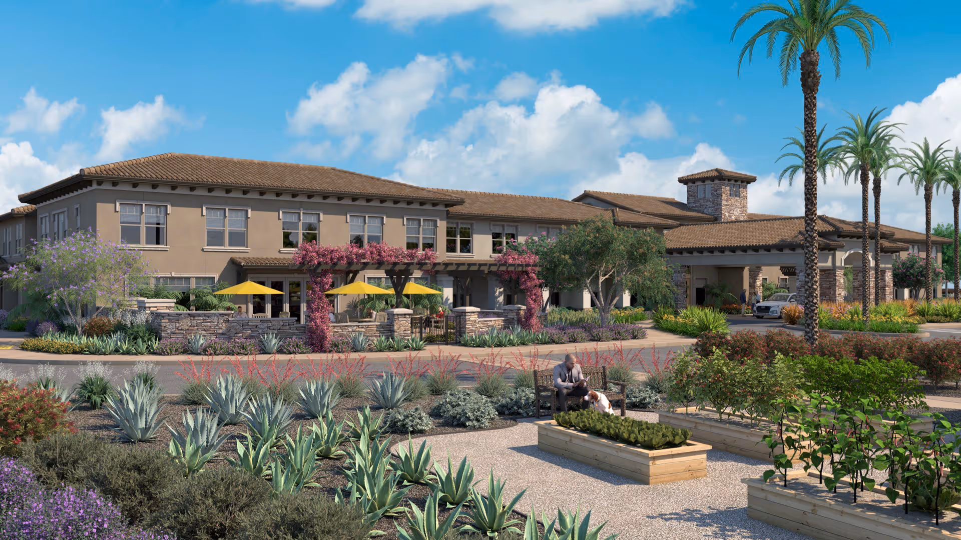 Front exterior of a Mediterranean-style senior living building with landscaped gardens, raised planter beds, palm trees, patio seating with yellow umbrellas, and a driveway.