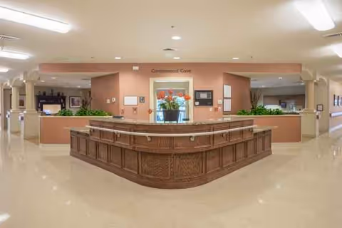 Interior view of a senior living lobby with a curved wooden front desk and plants.