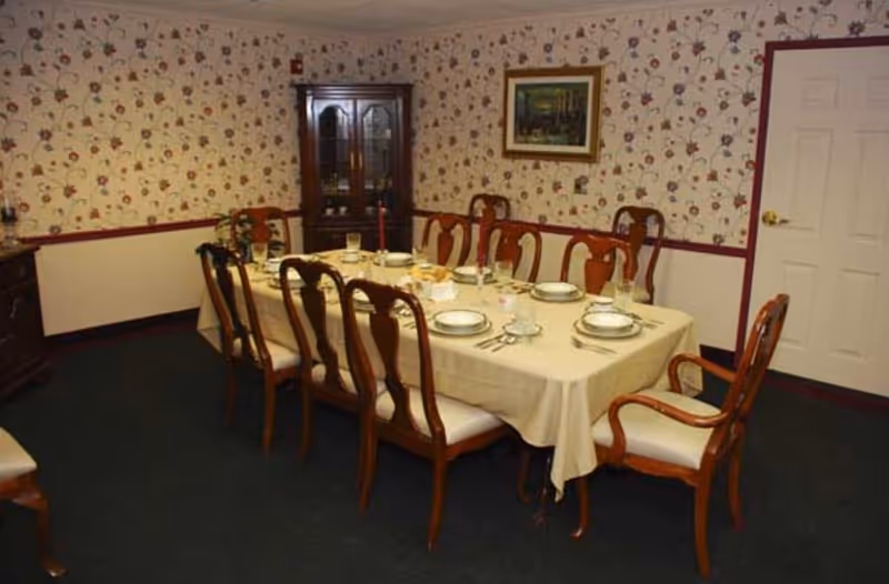Formal dining room with a table set for eight, wooden chairs, a china cabinet, and floral wallpaper.