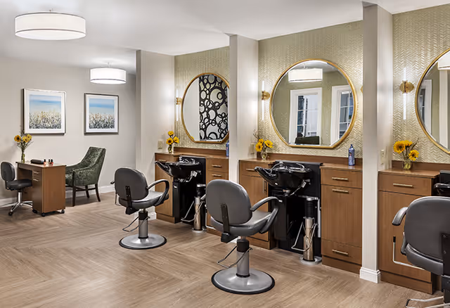 Bright, modern salon area with styling chairs, shampoo sinks beneath round mirrors and a small seating/desk area.