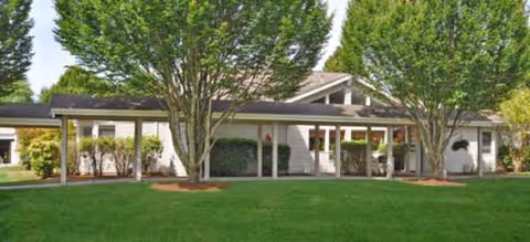 Single-story senior living facility with a covered entrance, manicured lawn, and trees.