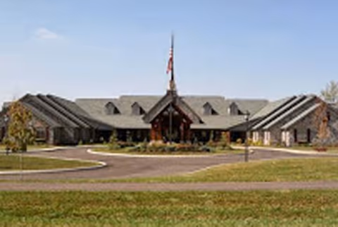 Front view of a low, stone senior living building with central entrance and flagpole.
