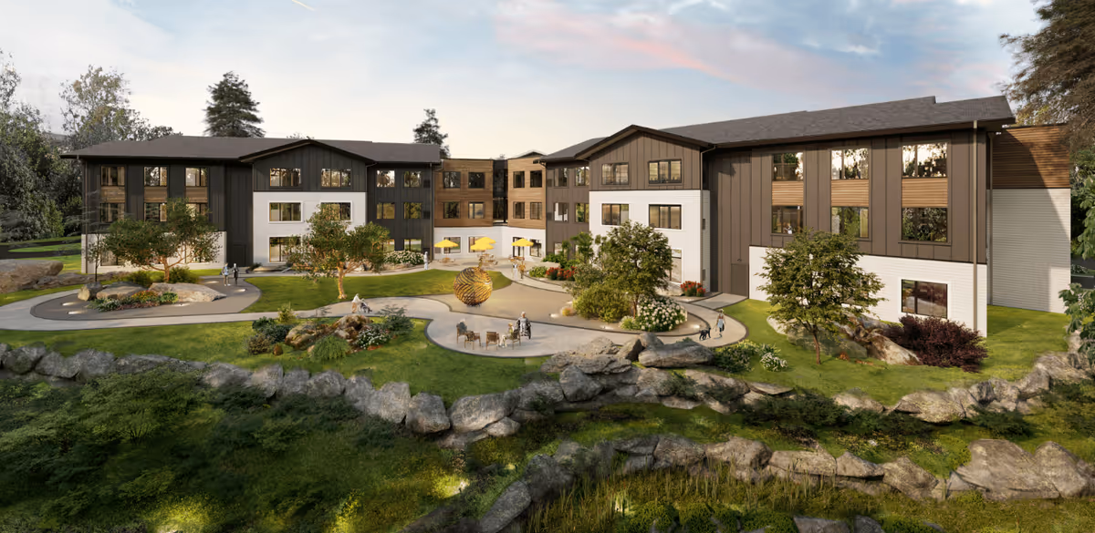 Exterior view of a modern three-story senior living facility named The Gallery at Spokane, featuring landscaped gardens, walking paths, trees, outdoor seating areas with people, and decorative sculptures under a partly cloudy sky.