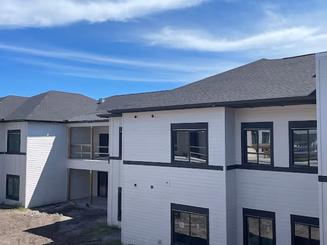 Exterior view of a two-story building with white siding and black trim under a blue sky with some clouds. The building has multiple windows and a covered walkway on the second floor.