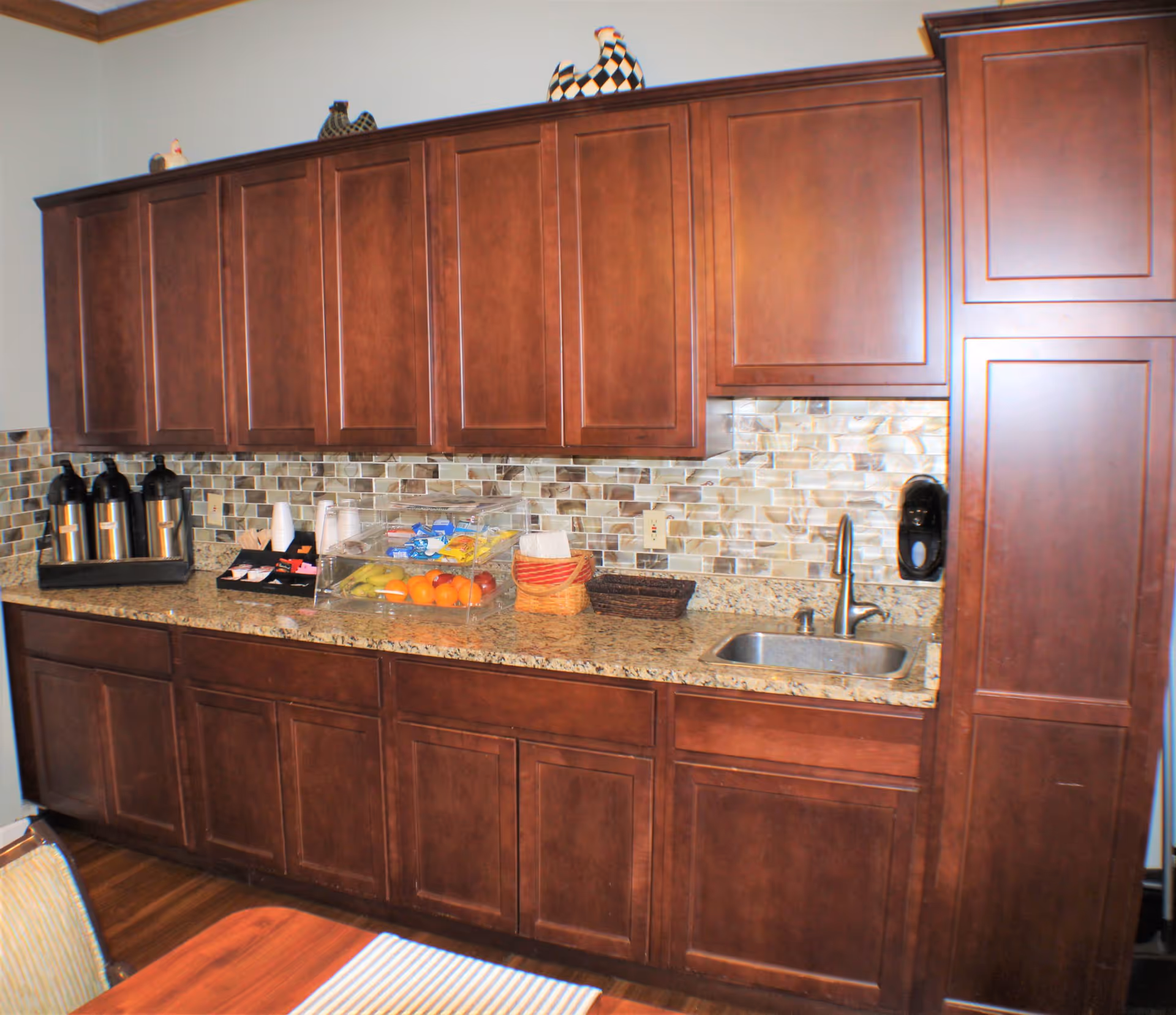 Kitchenette with dark wood cabinets, granite countertop, mosaic tile backsplash, sink, and a coffee/snack station.