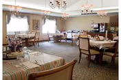 Assisted living dining room with several set tables and chairs, chandeliers, and a buffet station by the windows.