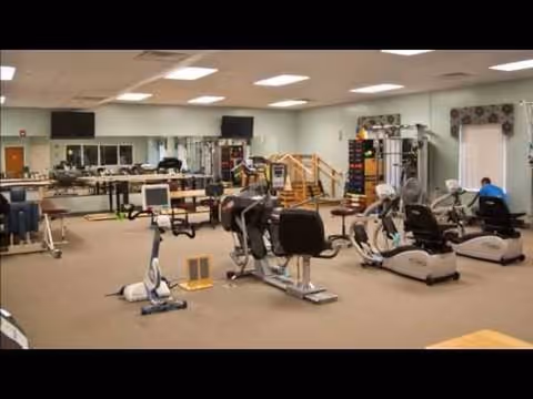 Rehabilitation gym in a senior facility with exercise bikes, treadmills, and residents exercising.