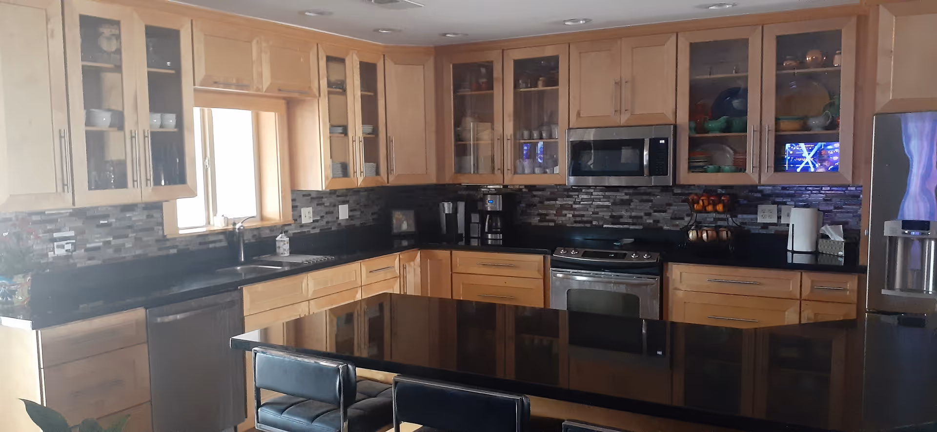 Modern kitchen with light wood cabinets, black countertops, stainless steel appliances and a large central island with stools.