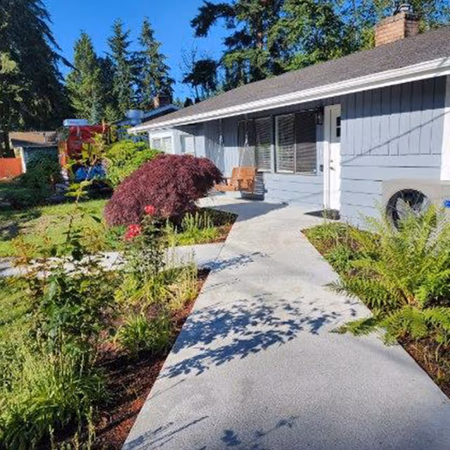 Front walkway leading to the entrance of a single-story gray house with landscaped garden and a porch swing.